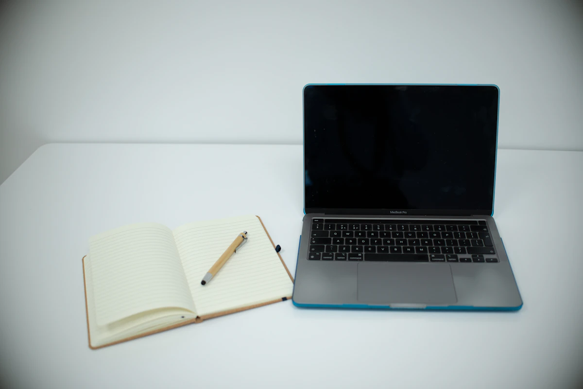 Foto ilustrasi buku catatan terbuka di samping laptop.